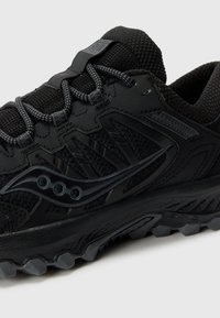 Chaussure de sport noire avec un upper en mesh texturé, des accents synthétiques, une semelle à motifs et un logo bien en vue sur le côté.