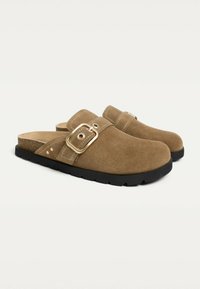 Brown suede clogs with a wide strap and gold buckle accent; black rubber sole with a textured underside for grip.