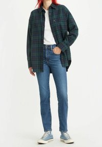 Camisa de cuadros verde y azul marino, camiseta blanca, jeans azules y zapatillas de lona azul claro. La camisa tiene un bolsillo en el pecho y un corte casual.