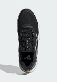 Zwart sportschoen met een gestructureerd bovenwerk, vetersluiting, gevoerde kraag en een witte zool. Heeft een logo op de tong en drie streepaccenten.