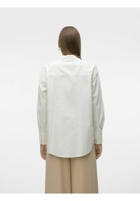 Camisa blanca de botones con cuello y mangas largas, con un dobladillo recto. La tela parece suave con detalles mínimos.