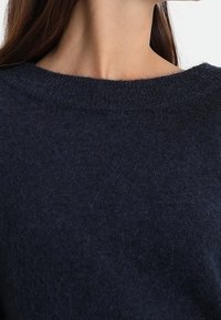 Laivastonsininen neulepusero, jossa on leveä pyöreä kaula-aukko. Pehmeä tekstuuri, jossa on hieman pörröinen pinta, rento malli ja ilman näkyviä koristeluja.