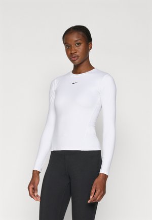 Witte sporttop met lange mouwen en een aansluitend ontwerp, met een zwart Nike-logo op de borst en een soepele textuur. Gepromoot met zwarte leggings.
