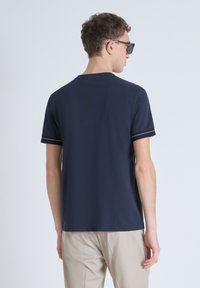 T-shirt a maniche corte di colore blu navy con scollatura rotonda e cuciture bianche a contrasto sui polsini, abbinato a pantaloni beige chiaro.
