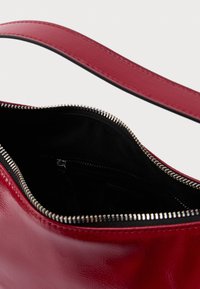 Κόκκινη τσάντα χειρός από συνθετικό δέρμα με κλείσιμο με φερμουάρ. Η εσωτερική επένδυση είναι από μαύρο ύφασμα και διαθέτει μικρές τσέπες για οργάνωση.