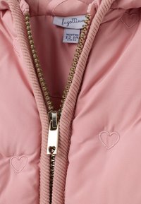 Veste doudoune rose avec une texture à pois, fermeture éclair dorée avec un détail en forme de cœur, et cœurs brodés sur la poitrine. L'étiquette indique une taille de 12-18 mois.
