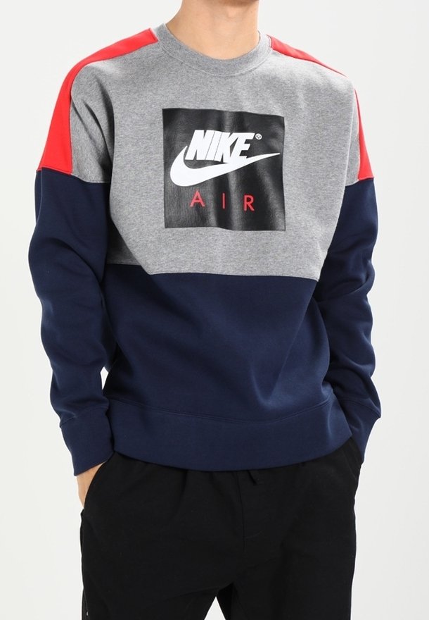 Nike sweatshirt med grå bomullstyg, röda axeldetaljer och en marinblå underdel. I mitten av logotypen står "NIKE AIR" i svart.