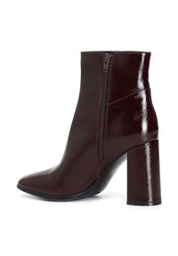 Burgundské kotníkové boty s lesklým, texturovaným povrchem. Disponují špičatou špičkou a bočním zipem. Silný, vysoký podpatek pro přidání výšky.