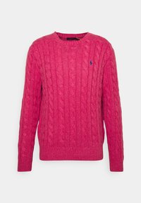 Pull rose en maille torsadée avec col rond, poignets et ourlet côtelés, arborant un petit logo bleu sur la poitrine. Texture douce.