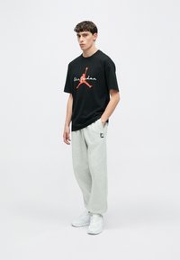 Μαύρο μπλουζάκι με λευκό και κόκκινο λογότυπο "Air Jordan", συνδυασμένο με ανοιχτό γκρι φόρμα και λευκά αθλητικά παπούτσια, με άνετη εφαρμογή.