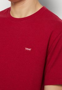 Červené bavlněné tričko s kulatým výstřihem a krátkými rukávy, s malým vyšívaným logem Levi's na hrudi. Hladká textura.