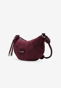 Bolso de ante burdeos con forma curva, cierre ajustable con cordón, herrajes plateados y un pequeño parche de logo negro.