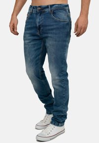 Vervaagde blauwe denimjeans met een slim fit, vijf-pocket ontwerp en contrasterende stikseldetails, gecombineerd met witte sneakers.