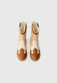 Brown and cream leather ankle boots with decorative cutouts, textured fabric lining, and side zippers for easy wear.