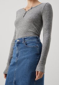 Grau gerippter Langarm-Oberteil mit einem Henley-Ausschnitt und drei Knöpfen, kombiniert mit einem blauen Jeansrock, der einen vorderen Schlitz und Taschen hat.