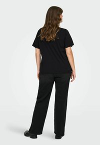 Black cotton t-shirt with short sleeves, worn with black wide-leg jeans. Model has medium-length wavy hair, viewed from the back.