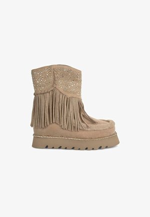 Beige suede ankle boot with fringe detail, perforated upper, decorative studs, and a low platform with a textured sole.