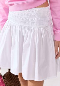 Gonna bianca con vita arricciata, caratterizzata da un design svasato. Il tessuto è leggero e liscio, creando pieghe fluenti.