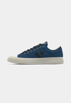 Blå lærreds sneakers med en hvid gummitosse; har sort stjerne- og chevronlogo, flade snørebånd og en tekstureret sål.