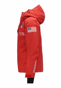 Giacca impermeabile rossa con cappuccio, caratterizzata da un logo visibile, una patch con la bandiera americana e polsini elastici con un rivestimento interno nero.