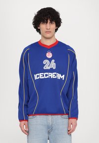 Blauwe longsleeve trui met rode kraag, voorzien van witte "ICECREAM" tekst en het nummer "24," aangevuld met gele stiksels.