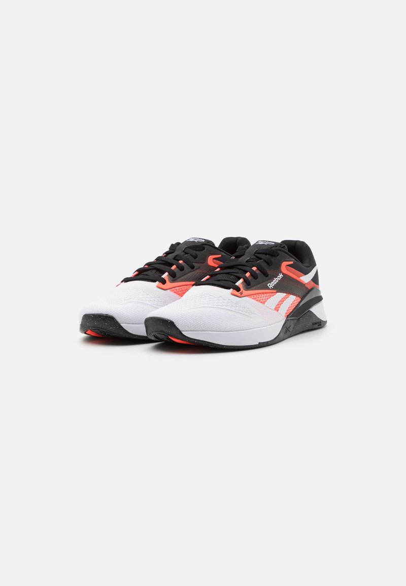Zapatillas blancas con acentos en negro y naranja neón, que cuentan con una parte superior de malla texturizada, cierre con cordones y una suela de goma con un patrón moteado.