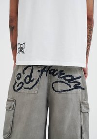 White T-shirt with a small black logo at the hem and gray cargo shorts featuring large black script on the back pockets.