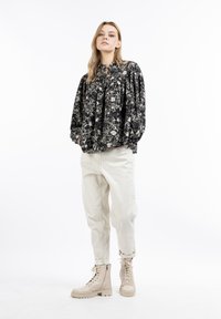 Black floral blouse with puffed sleeves, paired with light beige relaxed-fit pants and tan lace-up boots. Simple, modern design.