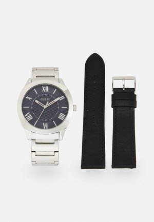 Montre en métal argenté avec un cadran à motif bleu foncé, des chiffres romains argentés et un bracelet à maillons argentés assorti ; comprend un bracelet en cuir noir.