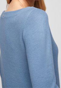 Jasnoniebieski dzianinowy sweter z okrągłym dekoltem, z małym guzikiem z tyłu oraz fakturowanym materiałem.