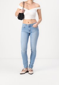 Vaqueros pitillo azul claro de cintura alta, combinados con una blusa blanca de hombros descubiertos y bailarinas beige con detalles de hebilla. Bolso negro incluido.