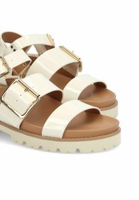 Witte gepatineerde leren sandalen met brede banden, voorzien van gouden gespen, een gevoerde tan binnenzool en een chunky witte zool met een textuur voor grip.