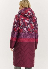 Pikowany długi płaszcz z mieszanymi wzorami kwiatowymi i geometrycznymi w odcieniach fioletu i burgundu. Projekt z kapturem, z fakturą jodełki u dołu.