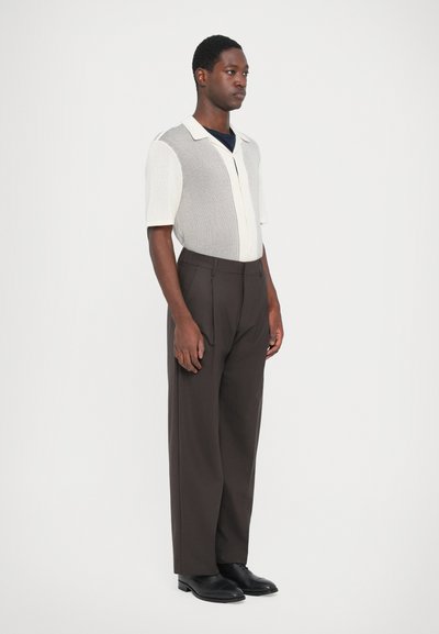 Knit short-sleeve polo shirt in white and gray, with a collar and buttons, paired with high-waisted dark brown trousers and black shoes.