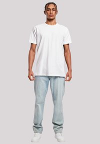 White cotton T-shirt with short sleeves, paired with light blue denim jeans. Features a classic fit and clean, simple design. White sneakers.