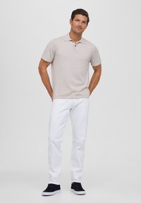 Polo de manga corta color beige claro con cuello y tapeta de dos botones, combinado con jeans rectos blancos y zapatillas navy.