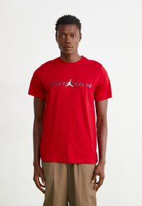 Rød bomulds t-shirt med et sort "JORDAN" logo og en hvid jumpman grafik. Kortærmet og med rund hals design.