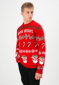 Rode gebreide trui met de tekst "Blissful Holidays", met groene hulst, witte sneeuwvlokken, suikerstokken en patronen van de Kerstman door het ontwerp.