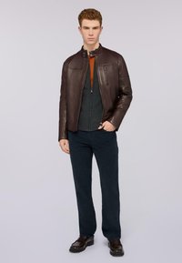 Hnědá kožená bunda s kapsami na zip, tmavě šedý svetr na zip, oranžové akcenty, námořnické kalhoty a hnědé boty. Jednoduchý, moderní design.