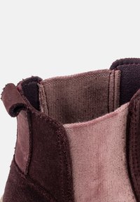 Burgundi színű velúr bokacsizmák puha textúrával, hátul húzófüllel és kontrasztos rózsaszín belső béléssel. Lekerekített felső szélek.