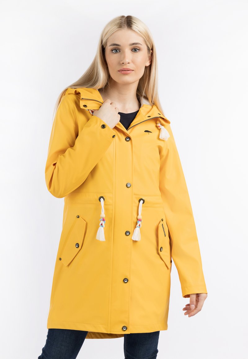Pelerina de raincoat galbenă, impermeabilă, cu glugă, multiple butoane, două buzunare frontale și ciucuri decorative la șnururi. Textură netedă și lucioasă.