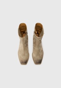 Scarpe ankle in suede color taupe con punta affusolata e zip laterale. Texture liscia con leggere sfumature dettagliate sulla punta. Logo visibile all'interno.