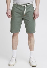 Pantalones cortos de algodón verde con una tela texturizada, que cuentan con una cintura ajustable con un diseño en blanco y negro, bolsillos laterales y un corte relajado.