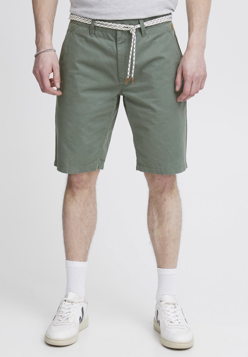 Pantalones cortos de algodón verde con una tela texturizada, que cuentan con una cintura ajustable con un diseño en blanco y negro, bolsillos laterales y un corte relajado.