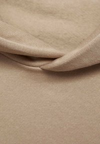 Tessuto a maglia beige con cucitura visibile e bordo piegato, che mostra in primo piano la texture e il motivo di tessitura.