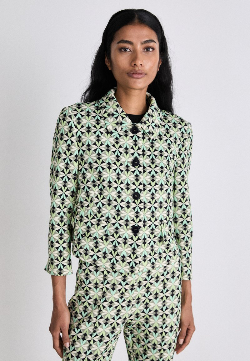 Gemusterte Jacke mit schwarzem Hintergrund, die ein geometrisches Design in Minzgrün und Creme zeigt. Sechs schwarze Knöpfe und ein Kragen.