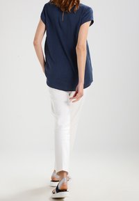 Námořnická modrá, krátký rukáv, top s texturovaným vzorem, spárovaný s bílými, slim-fit kalhotami; model nosí stříbrné a modré sandály.