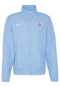 Ljusblå jacka med hög krage, tryckknappar, elastiska ärmar och nederkant. Har en röd och vit tjurlogotyp samt en vit Nike-swoosh.