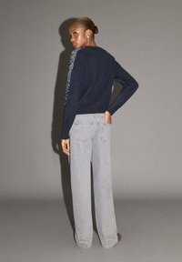 Maglione navy con decorazioni testurizzate sulle maniche, abbinato a jeans a gamba larga grigio chiaro, che mette in risalto un fit rilassato e dettagli sottili.