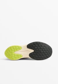 Semelle de chaussure présentant une surface texturée noire avec des crampons proéminents, une section centrale de couleur beige clair et un accent vert lime vif.